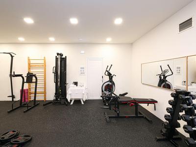 Kleiner Fitnessraum mit verschiedenen Trainingsgeräten und Spiegel an der Wand.