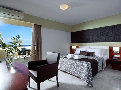 Modernes Hotelzimmer mit großem Bett, Sitzgelegenheit und Balkon mit Meerblick.