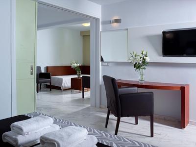 Moderner Hotelraum mit Schreibtisch, Stuhl und angrenzendem Sitzbereich mit Sofa.