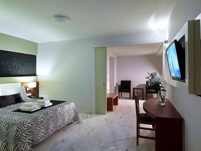 Helles Hotelzimmer mit Doppelbett, Schreibtisch, Stuhl und Wandfernseher.