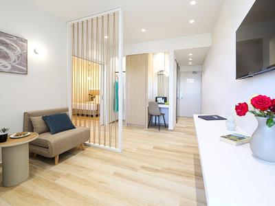 Modern eingerichteter Hotelraum mit Holzboden, Trennwand und Sitzecke mit Sofa und Tisch.