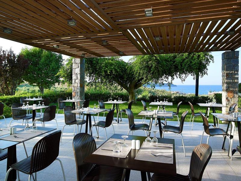 Moderne buitenruimte van een restaurant met uitzicht op tuin en zee.