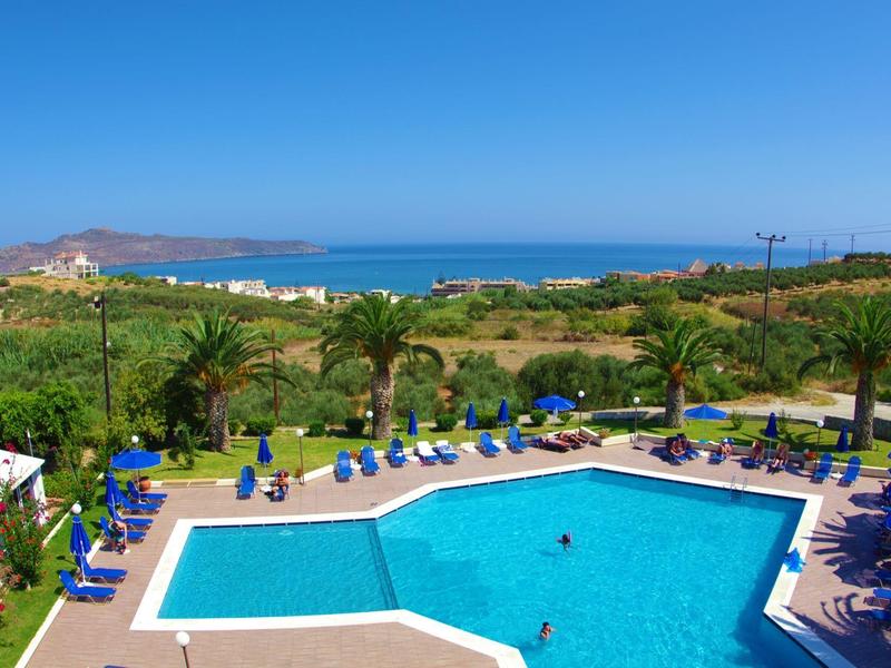 Zwembad met blauwe ligstoelen, groen landschap en zee onder een heldere hemel.