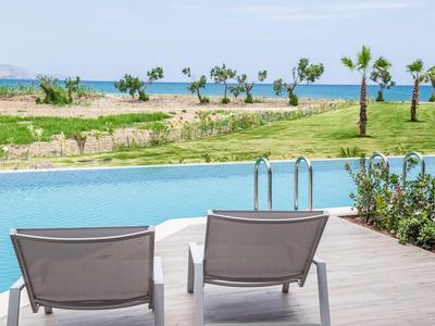 Two lounge chairs by the pool overlooking greenery and the sea in the background.