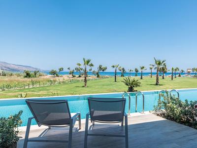 Two lounge chairs face a pool with palm trees and ocean in the background under a clear blue sky.