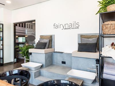Modern nail salon with gray pedicure chairs, white foot baths, and organized shelves with baskets.