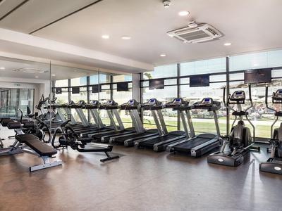 Spacious gym with treadmills, exercise bikes, and large windows overlooking green fields.
