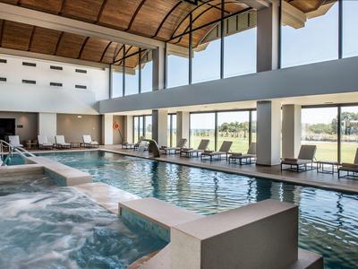 Indoor pool area with lounge chairs and large windows overlooking greenery.