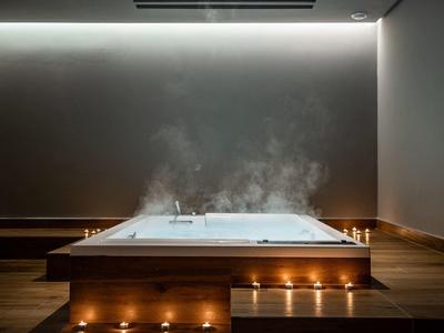 Steaming indoor hot tub with warm lighting and candles on a wooden platform.