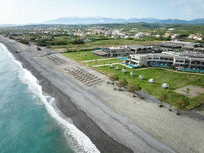 A resort hotel by a pebble beach with sunbeds and umbrellas on a green lawn.
