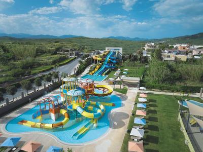 Wasserpark mit Rutschen, einem Kinderbecken und Liegestühlen neben einem Golfplatz.