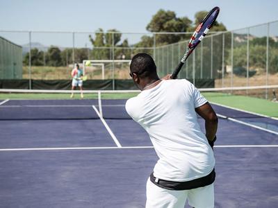 Zwei Männer spielen Tennis auf einem Freiluftplatz an einem sonnigen Tag.
