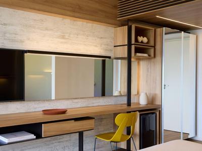 Modern hotel room with wooden furniture, a yellow chair, and a large mirror on the wall.