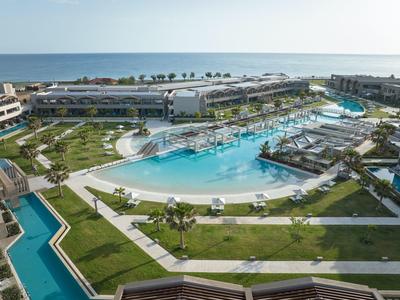 Large resort with curving pool, green lawns, palm trees, and distant ocean view