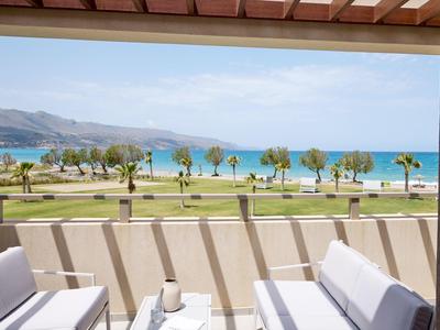 Balcony seating overlooking palm trees and a clear blue beach with mountains in the distance.