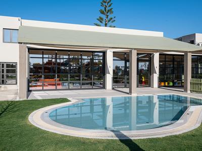 Modern hotel building with large windows next to a round swimming pool and green lawn.