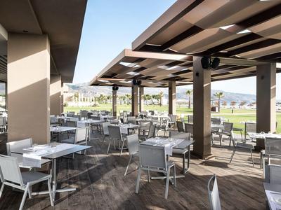 Outdoor hotel restaurant with modern tables and chairs under shaded pergolas.