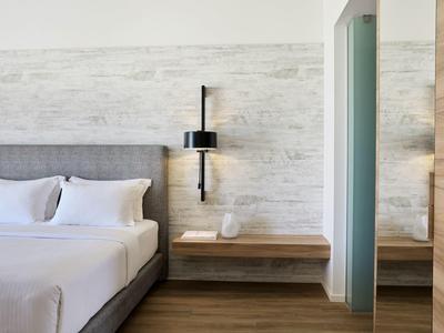 Modern hotel room with gray bed, white pillows, a black wall lamp, and wooden shelves