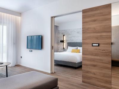 Modern hotel room with wooden sliding door, wall-mounted TV, and a white bed in the background.