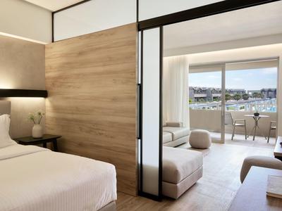 Modern hotel room with bed, wooden accents, and balcony overlooking water and buildings.