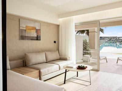 Modern eingerichtetes Hotelzimmer mit Sofa, Kaffetisch und Blick auf den Poolbereich.