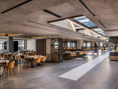 Spacious hotel dining area with wooden tables, beige chairs, and skylights.