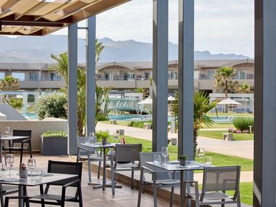 Outdoor seating area with tables and chairs overlooking a garden and pool with mountains in background.