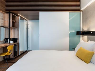 Modern hotel room with large bed, yellow chair, and wooden wall paneling