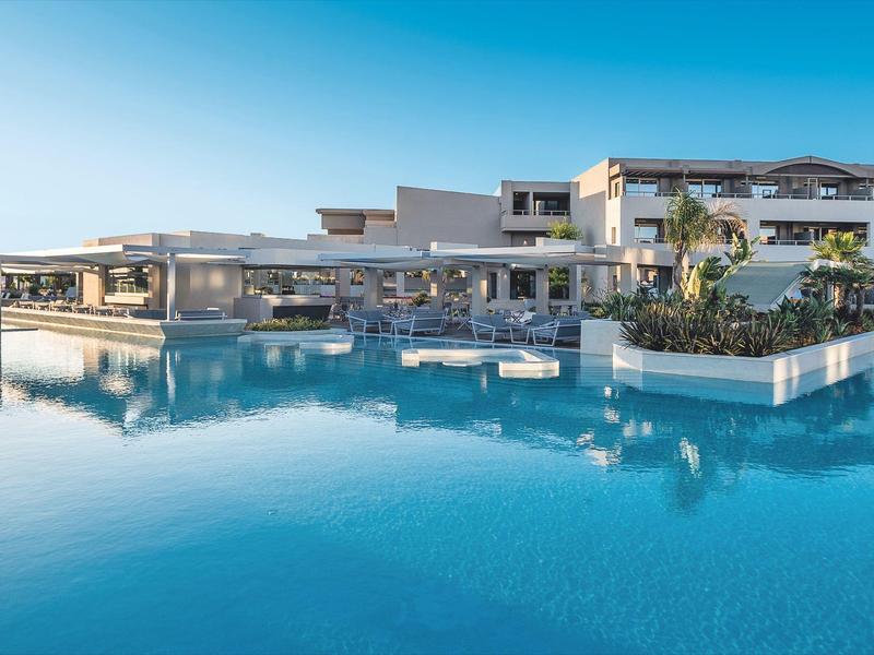 Modern hotel with large infinity pool reflecting the clear blue sky.