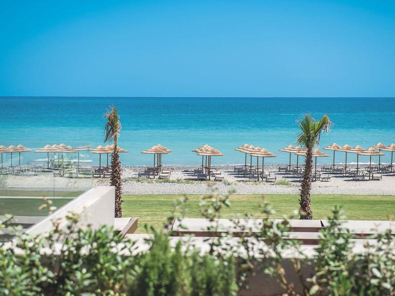 Beach with umbrellas, palm trees, and clear blue sea under a bright sky.