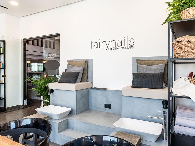 Modern nail salon with gray pedicure chairs, white foot baths, and organized shelves with baskets.