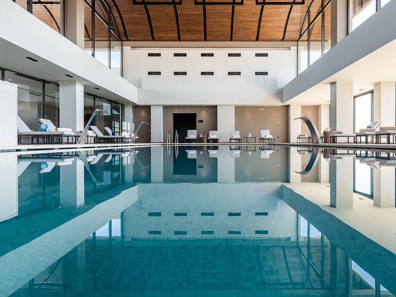 Modern indoor pool with clear water and wooden ceiling in a spacious hotel area.
