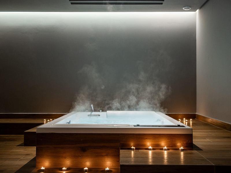 Steaming indoor hot tub with warm lighting and candles on a wooden platform.