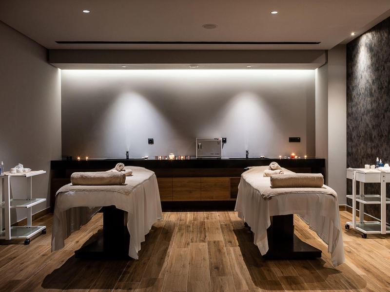 Calm spa room with two massage tables, soft lighting, wooden floor, and minimal decor.