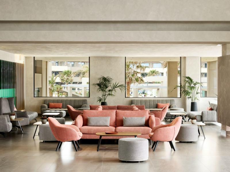 Modern hotel lobby with stylish pink and gray sofas, armchairs, and coffee tables.
