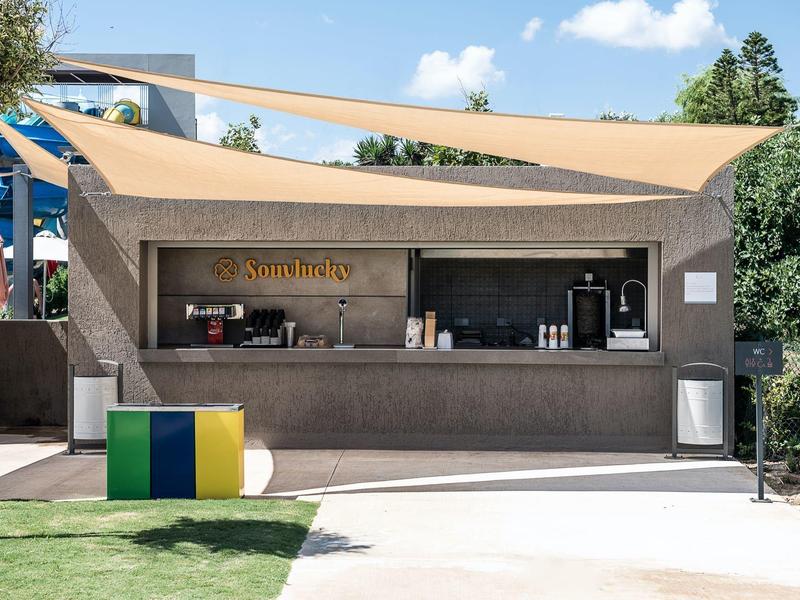 Outdoor snack bar with beige sail shade and colorful seating cubes on a sunny day