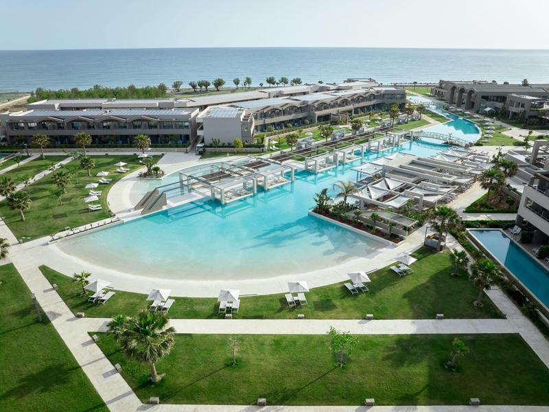 A luxury resort with large pools, sun loungers, palm trees, and ocean view.