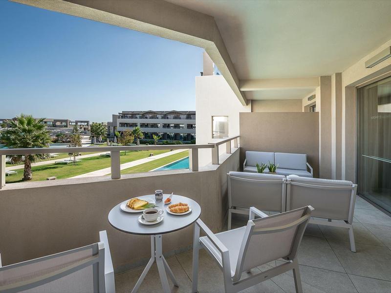 Balcony with chairs, table, and breakfast overlooking pool and buildings.