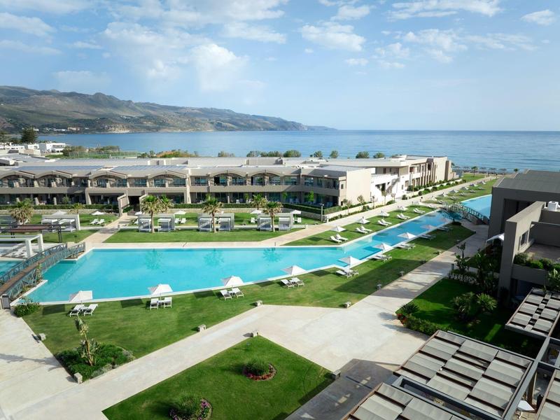 Beachfront resort with large pool, sunbeds, and ocean views under a blue sky.