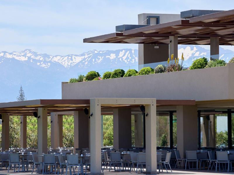 Mountain-view hotel terrace with outdoor seating under wooden pergolas on a clear day.