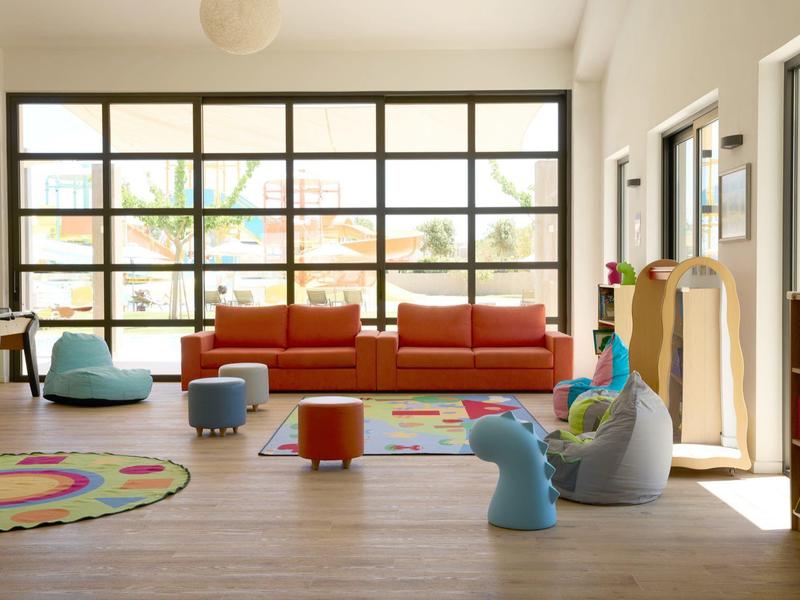 Bright, spacious children's playroom with large windows, colorful rugs, and soft seating.