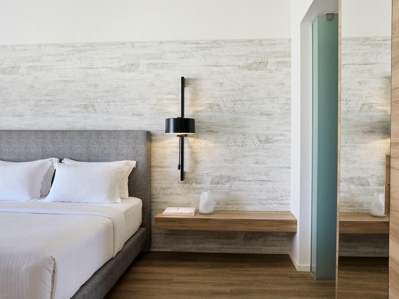 Modern hotel room with gray bed, white pillows, a black wall lamp, and wooden shelves