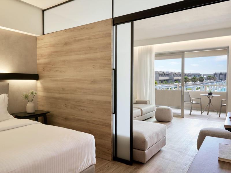 Modern hotel room with bed, wooden accents, and balcony overlooking water and buildings.