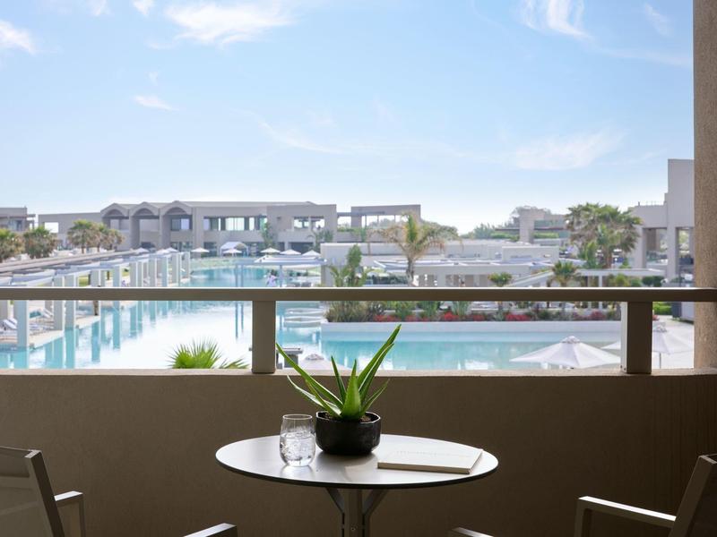 Balcony view of a resort pool area with clear blue sky and modern buildings.