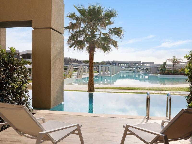 Pool view with lounge chairs, palm tree, and clear sky at a resort.