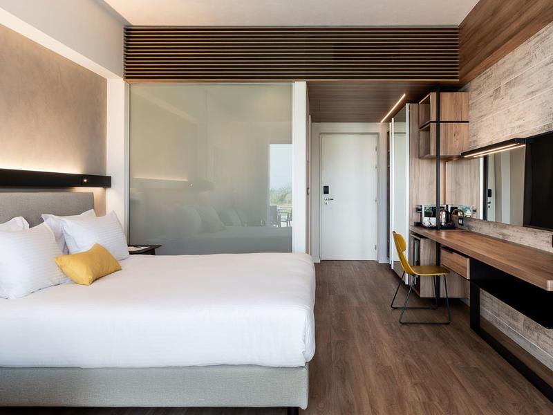 Modern hotel room with double bed, wooden floor, and wall-mounted TV.