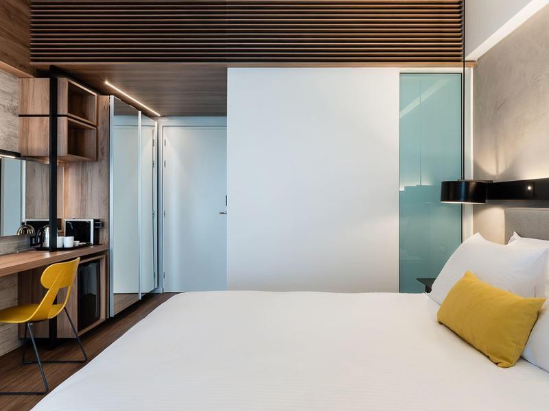 Modern hotel room with large bed, yellow chair, and wooden wall paneling
