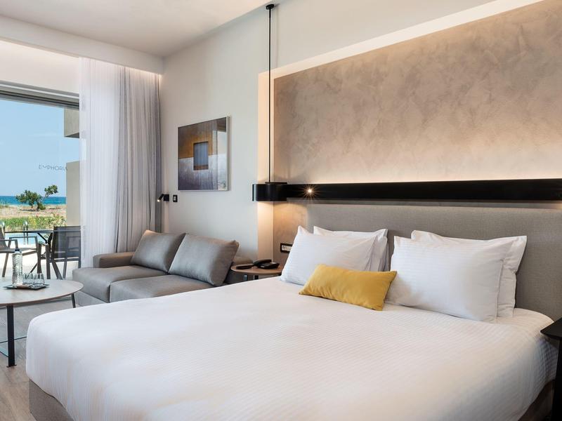 Modern hotel room with large bed, sofa, and balcony with sea view.