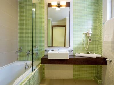 Bagno moderno con vasca da bagno, lavabo, specchio e asciugacapelli in piastrelle verde chiaro.