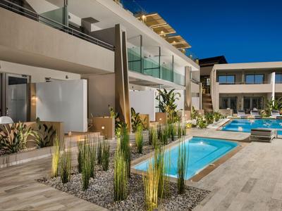 Area piscina di hotel moderna con piscine limpide, piante alte e ringhiere in vetro sotto un cielo azzurro